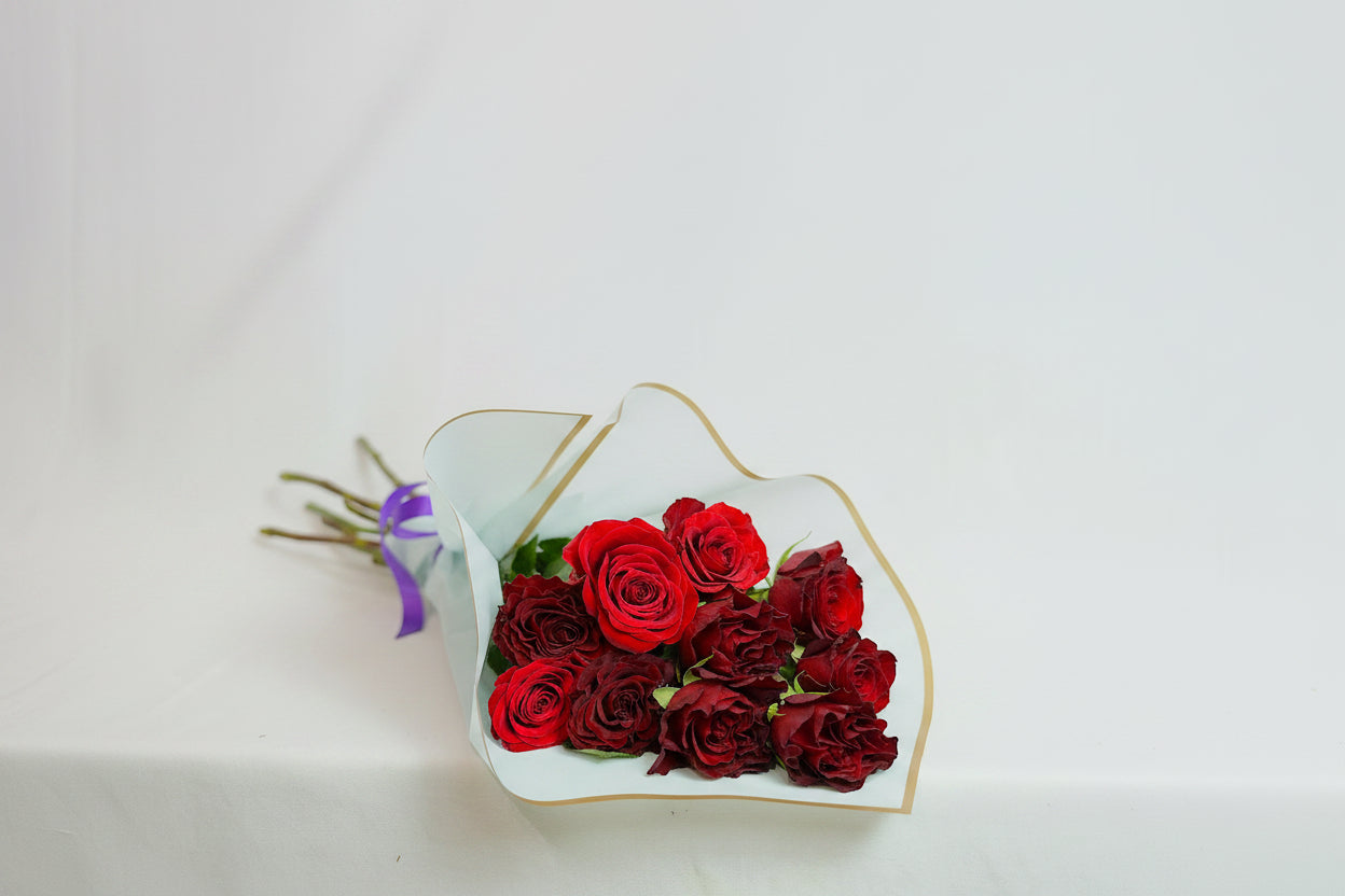 Bouquet of red roses wrapped in white paper with gold trim on a light gray background