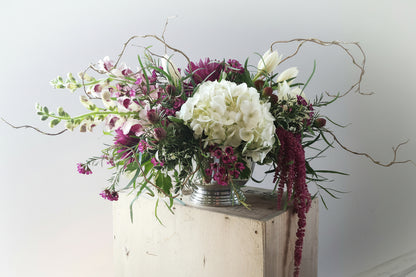 Floral arrangement with white and purple flowers on a wooden stand against a light background