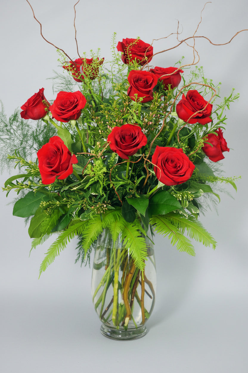 Bouquet of red roses in a clear vase with greenery on a white background