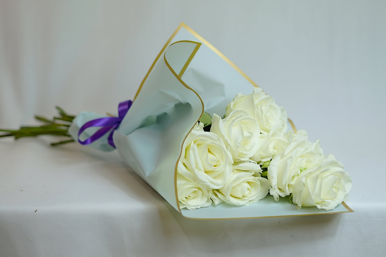 Bouquet of white roses wrapped in light green paper with gold edge on a white background