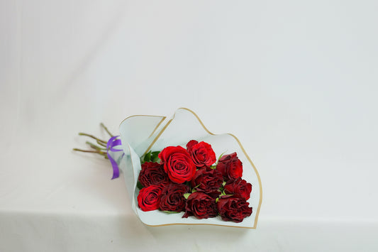 Bouquet of red roses wrapped in white paper with gold trim on a light gray background
