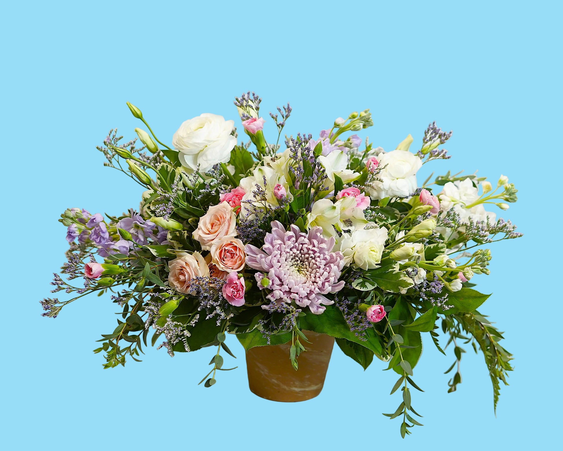 A vibrant floral arrangement featuring white roses, pink and peach roses, a light purple chrysanthemum, and green foliage, presented in a terracotta-colored pot against a plain white background.